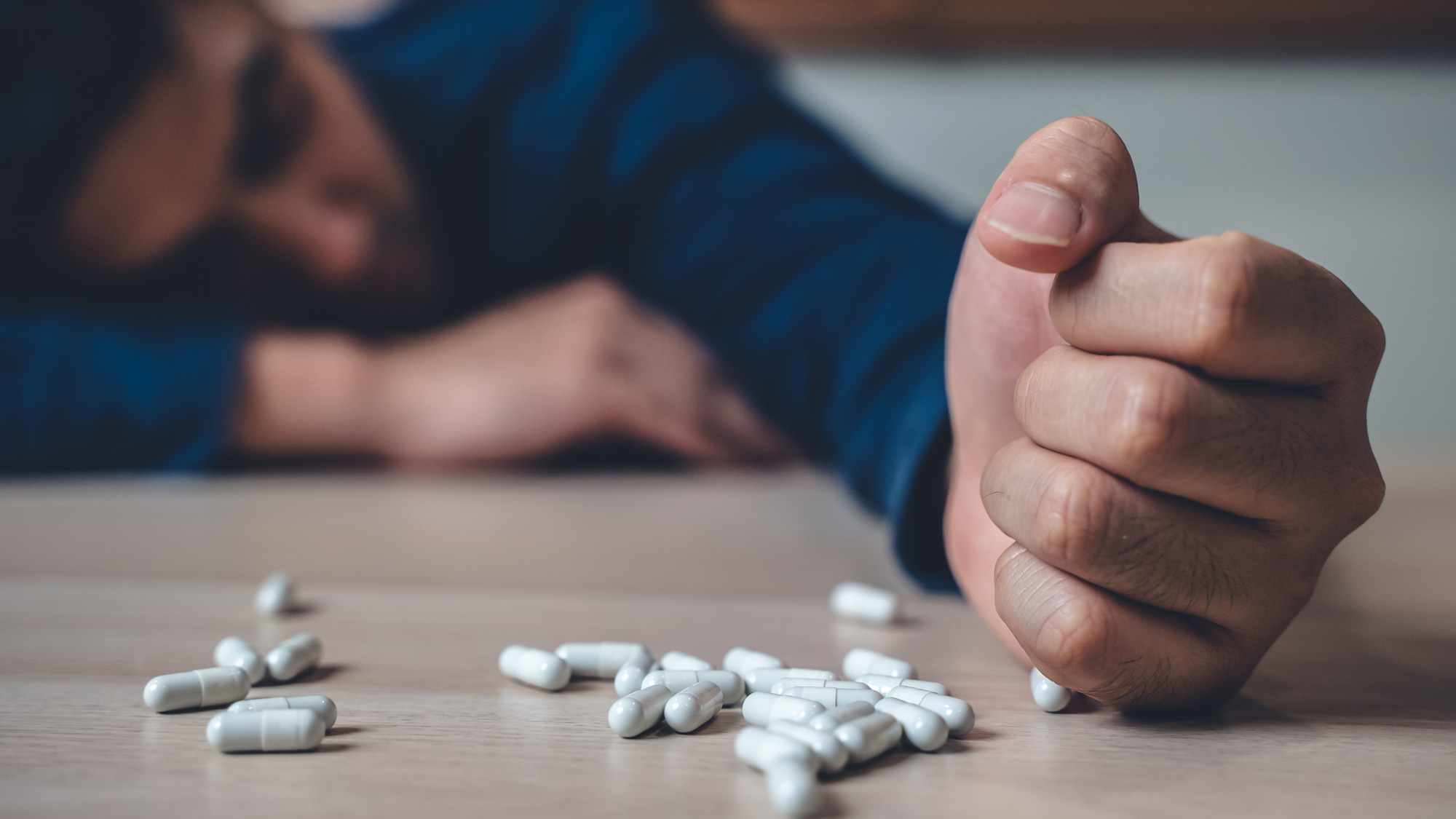 the person using drug overdoses lying on the table. close up on pills in hand.