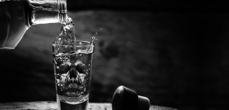 Drink bottle and glass with alcohol content. Image of translucent skull in glass.